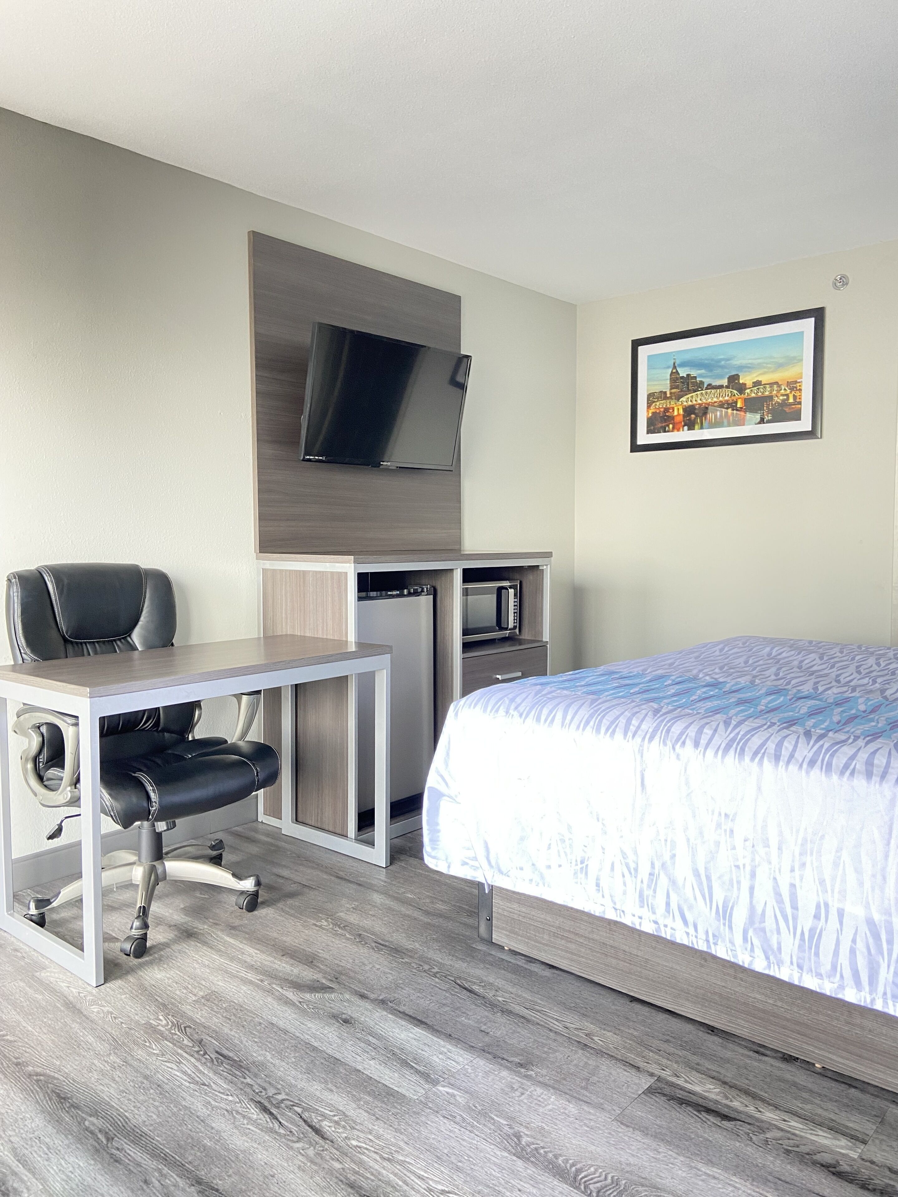 A hotel room with a bed, desk, chair, TV, and microwave.