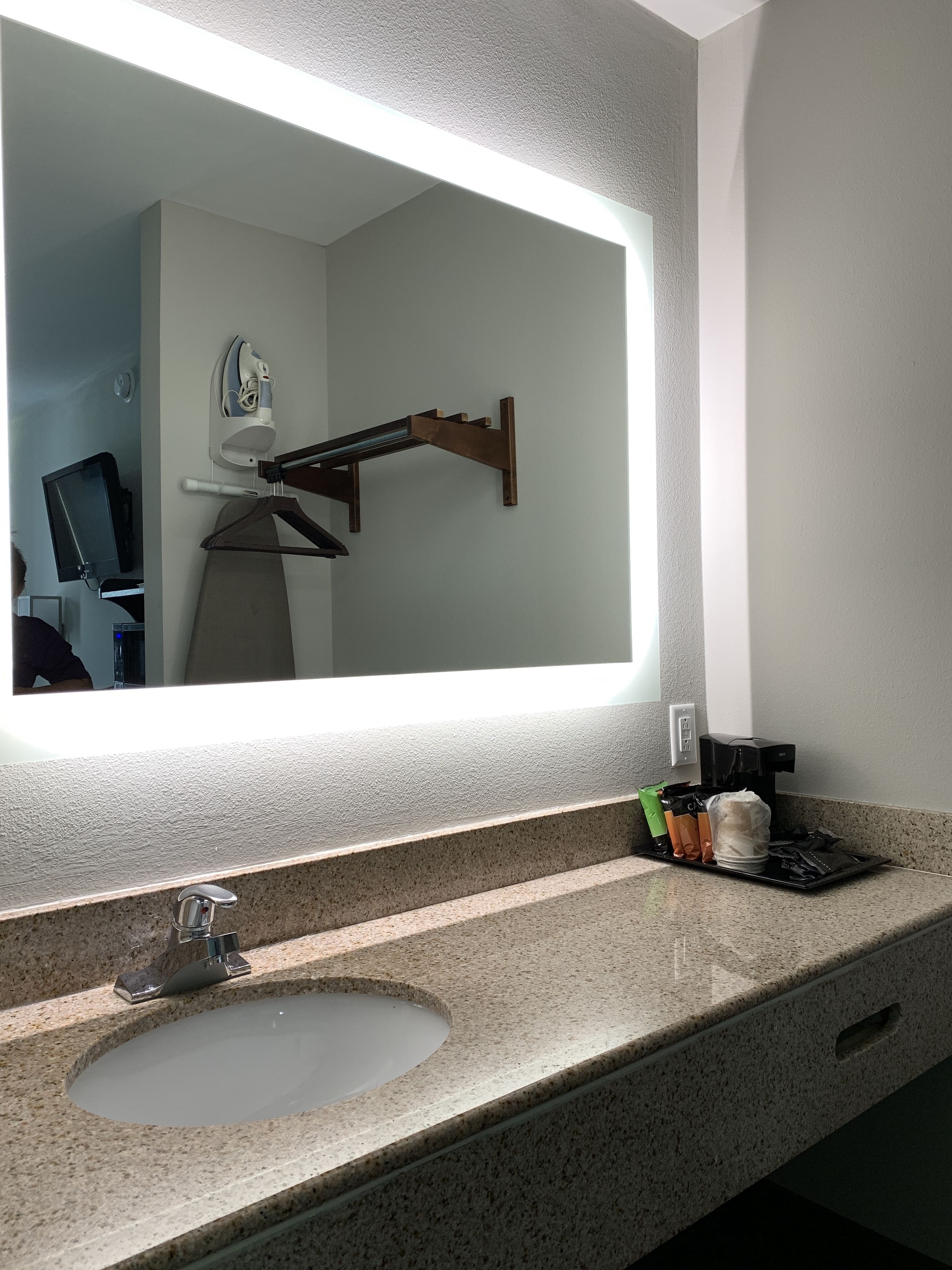 Un baño con un espejo grande, un lavabo y una cafetera.