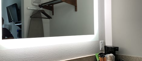 Een badkamer met een grote spiegel, een wastafel en een koffieapparaat.