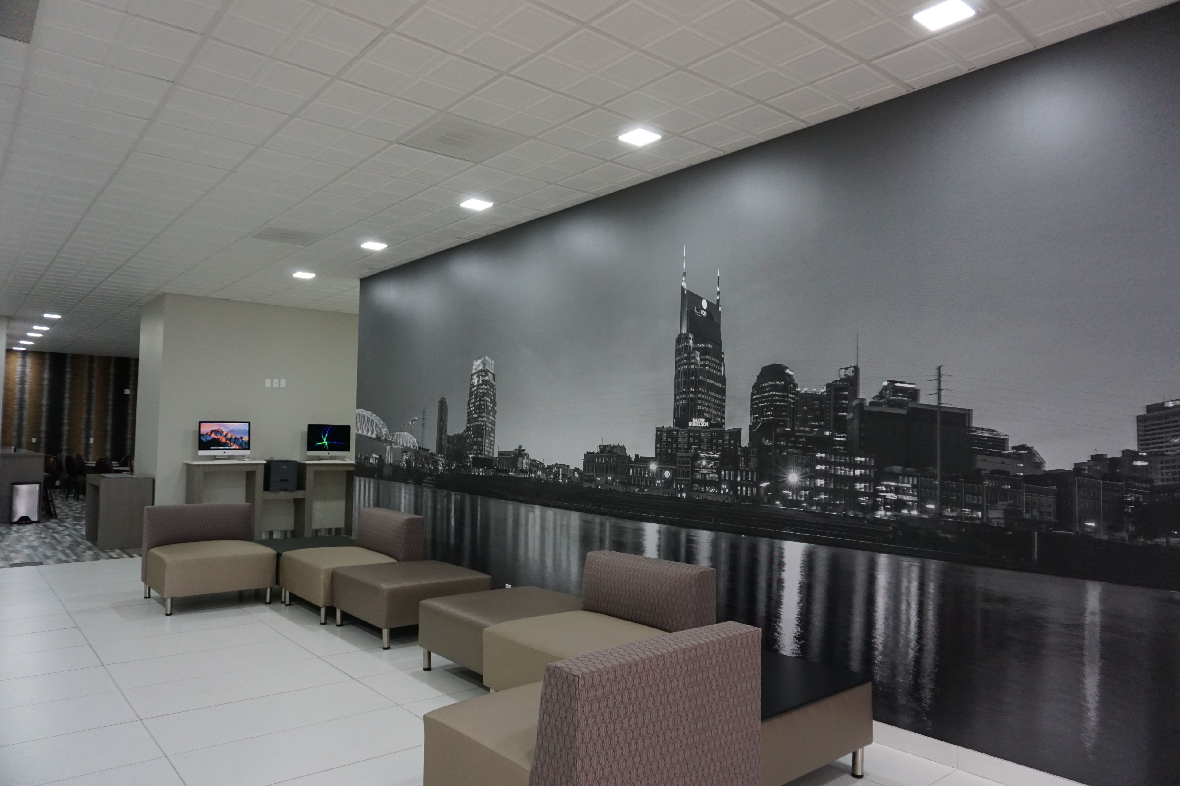 A modern hotel lobby with a cityscape mural, comfortable seating, and a flat-screen TV.