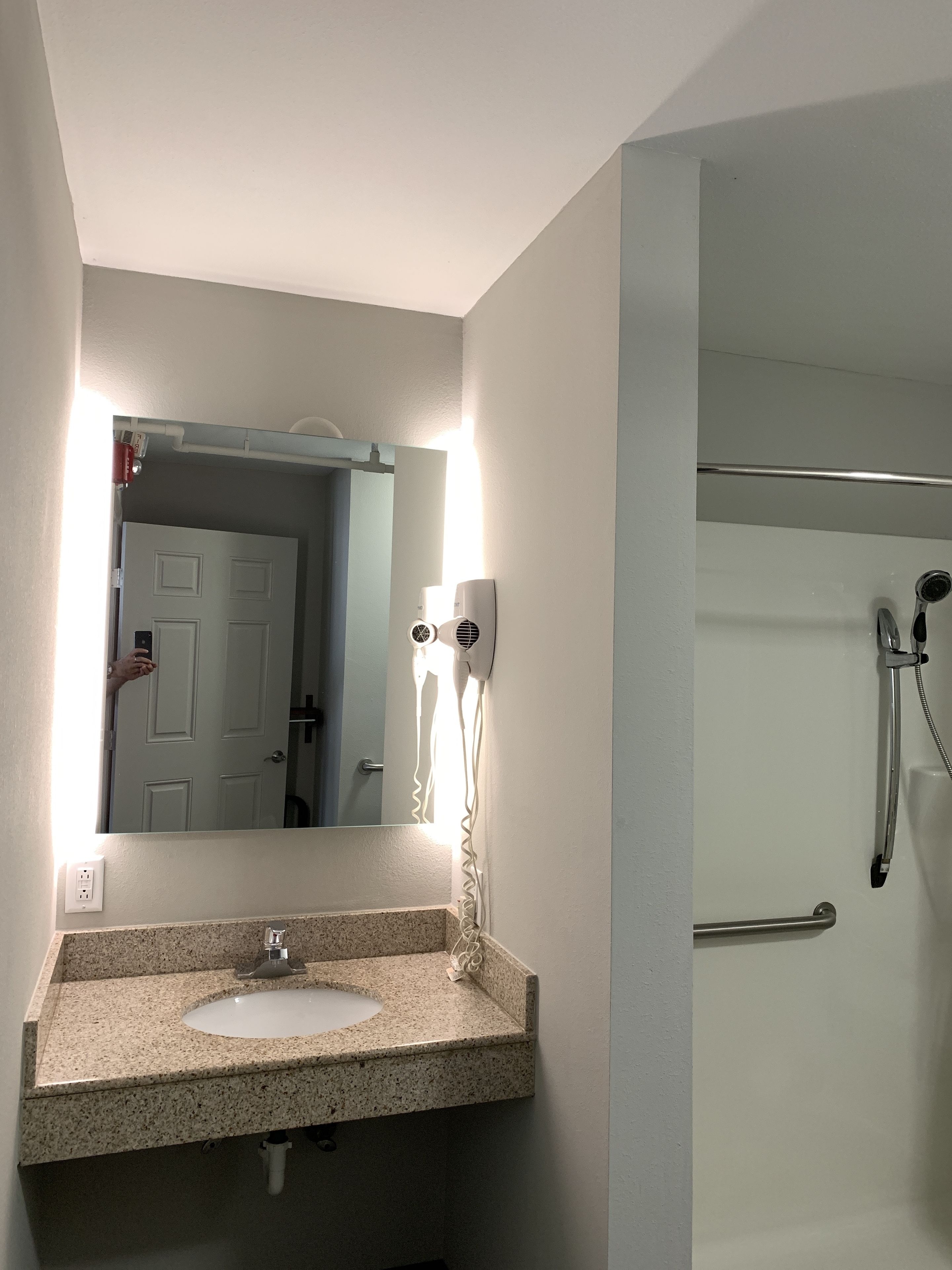 Baño con lavamanos de granito, espejo con luz, secador de pelo y ducha con barra de apoyo.
