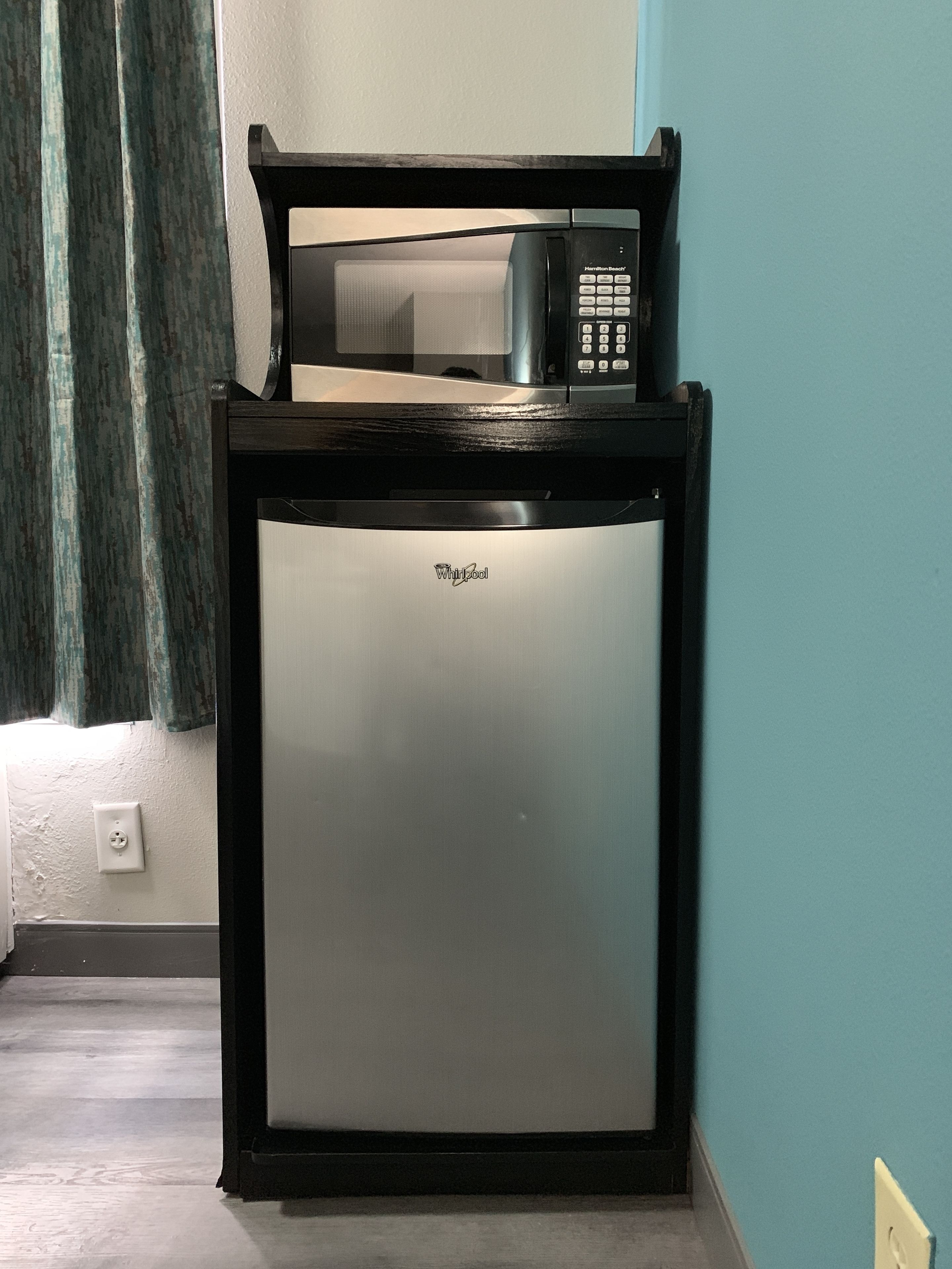 Un refrigerador compacto con un microondas encima, colocado frente a una pared verde azulada.