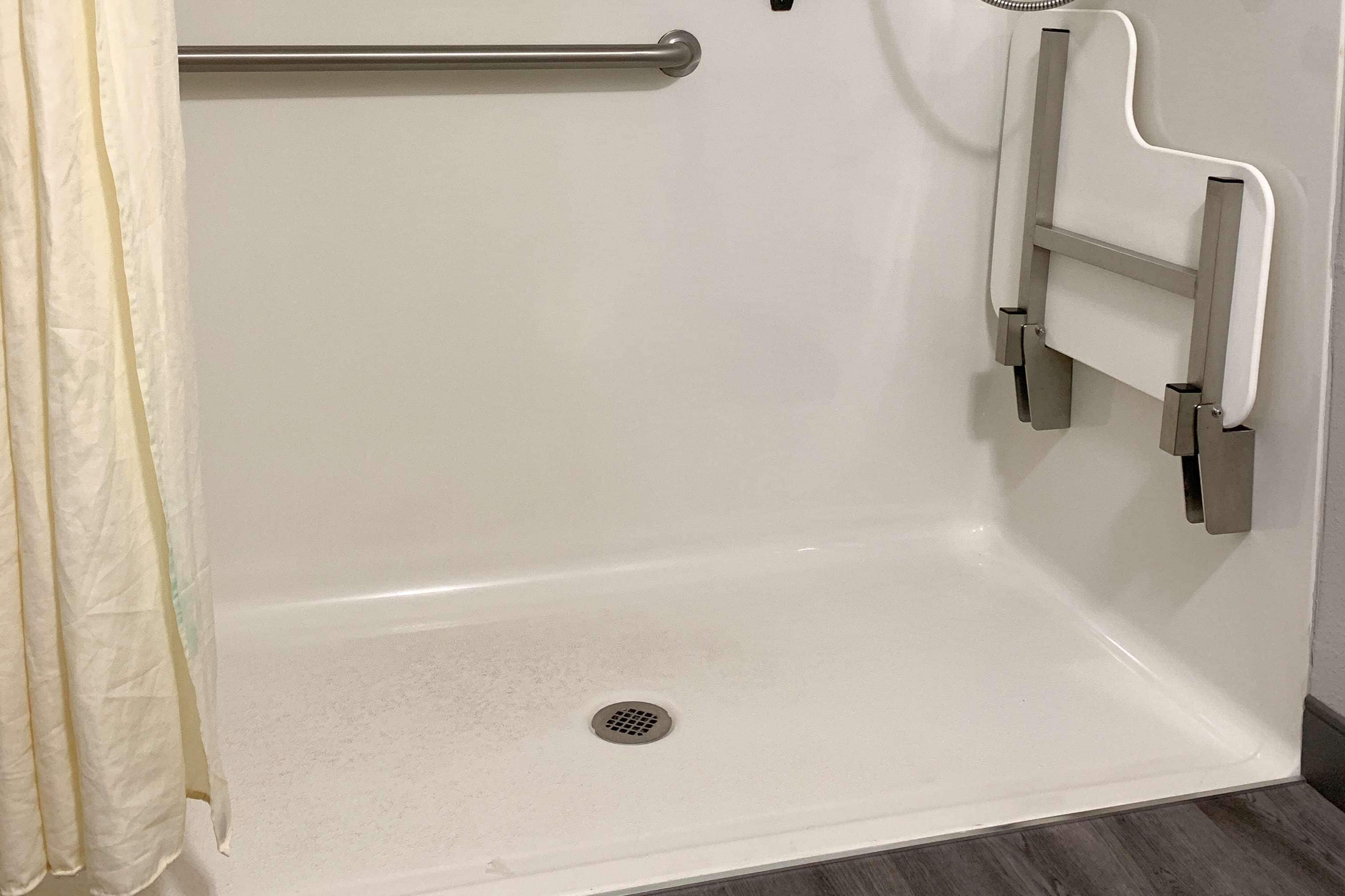 A white bathtub with a grab bar, a shower curtain, and a drain.