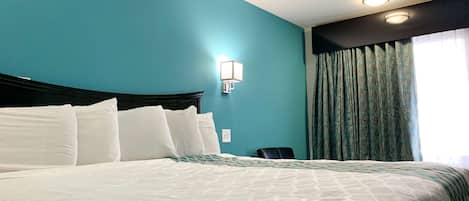 Una habitación de hotel con una cama grande, paredes color verde azulado, una lámpara de pared y un ventanal con cortinas.