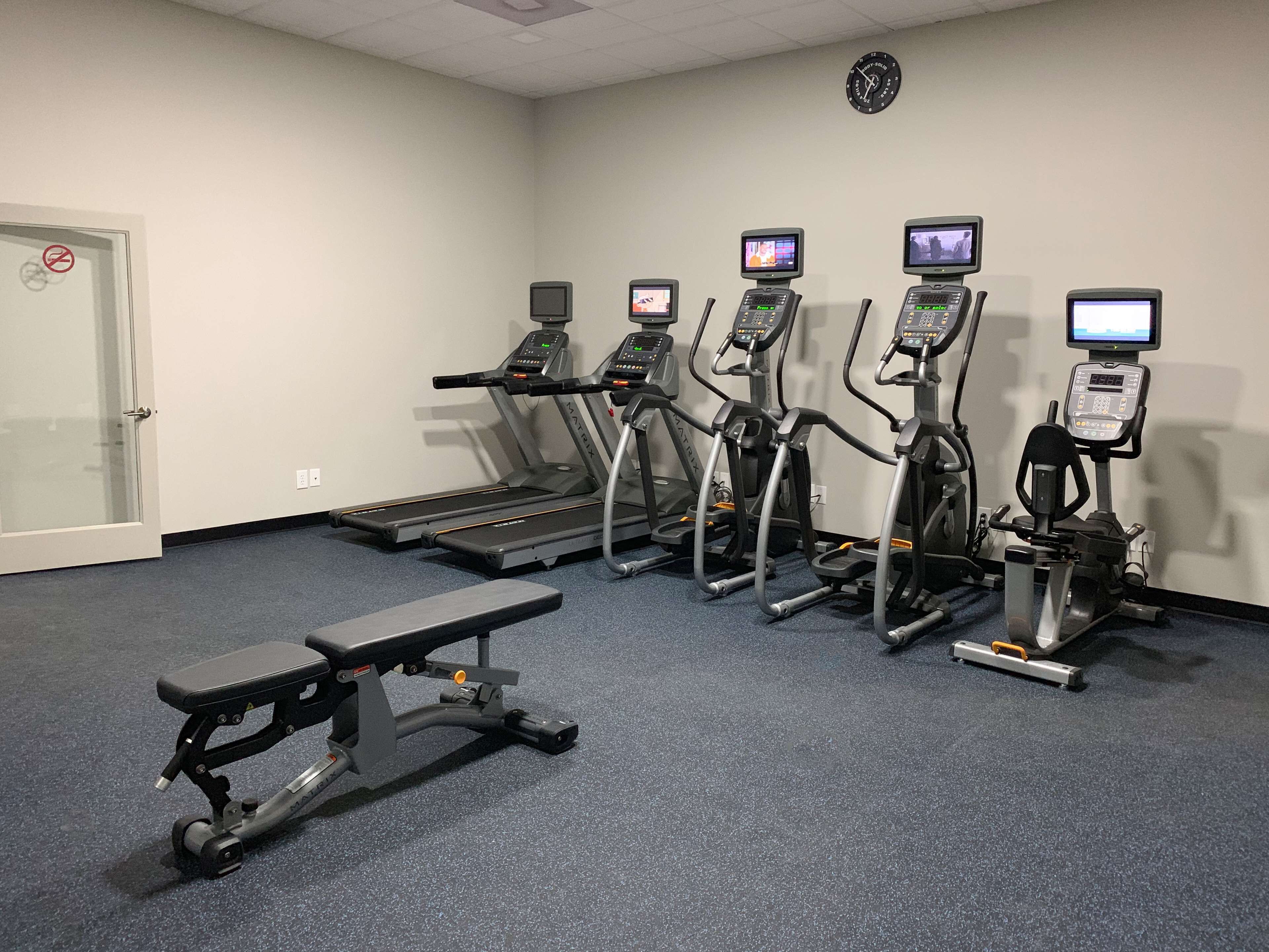 Ein Fitnessraum mit Laufbändern, Crosstrainern und einer Trainingsbank.