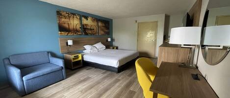 A hotel room with a bed, a sofa, a desk, and a chair.
