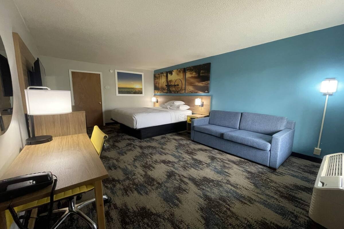 A hotel room with a bed, a sofa, a desk, and a lamp.