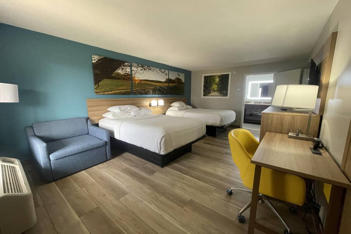 A hotel room with two beds, a desk, a chair, a sofa, and artwork on the walls.