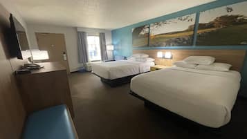 Habitación de hotel con dos camas, un escritorio con lámpara, un banco y un ventanal con cortinas.