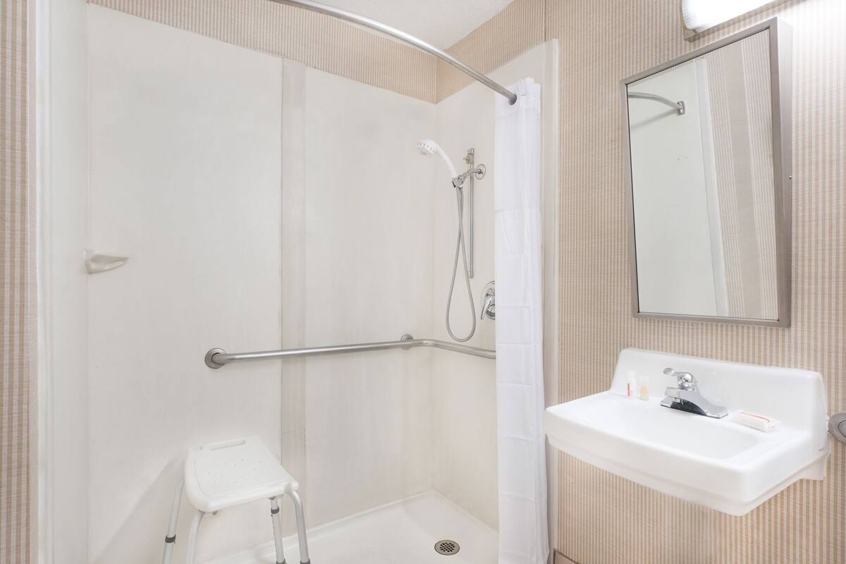 A shower with a grab bar, a white sink, and a mirror.