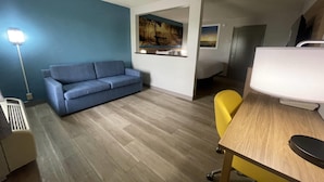 A room with a blue sofa, a yellow chair, a desk with a computer, a painting on the wall, and a lamp. - Days Inn & Suites by Wyndham York (York)