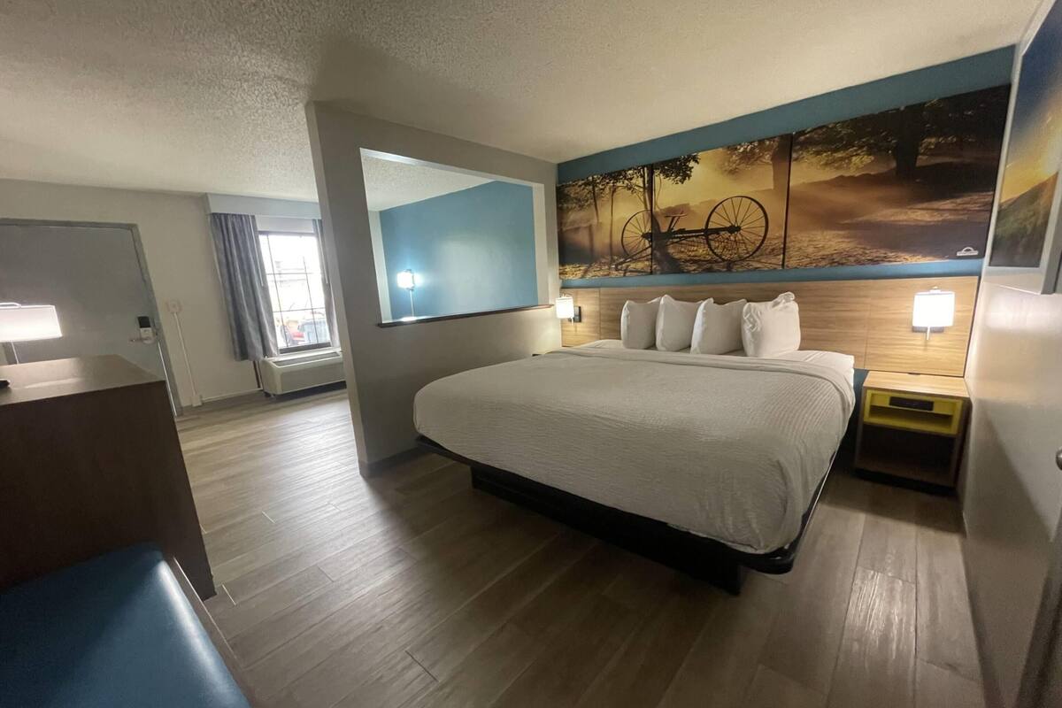 A hotel room with a large bed, a desk, a mirror, and a wall with a painting.