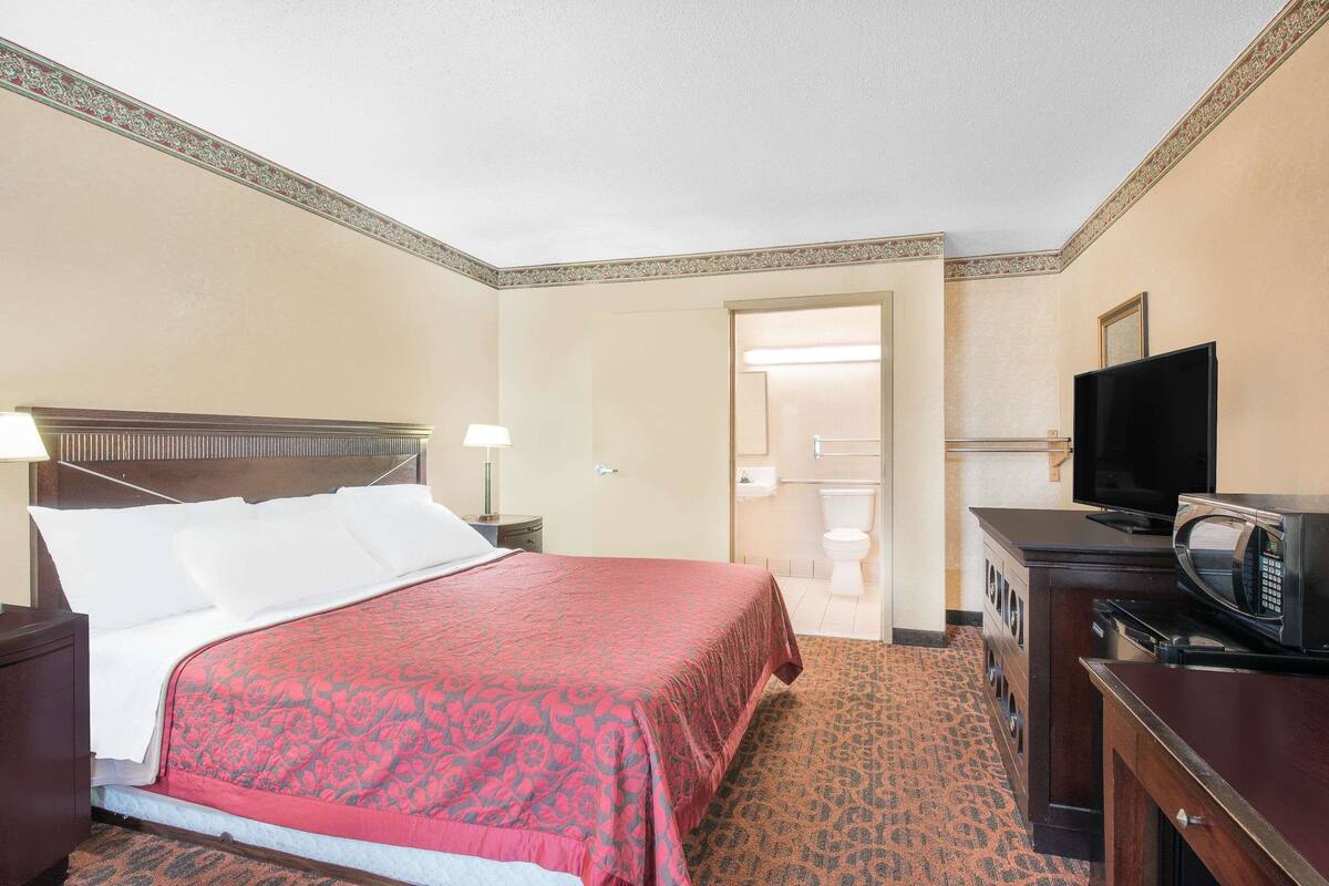 A hotel room with a bed, a television, a microwave, and a bathroom visible through an open door.