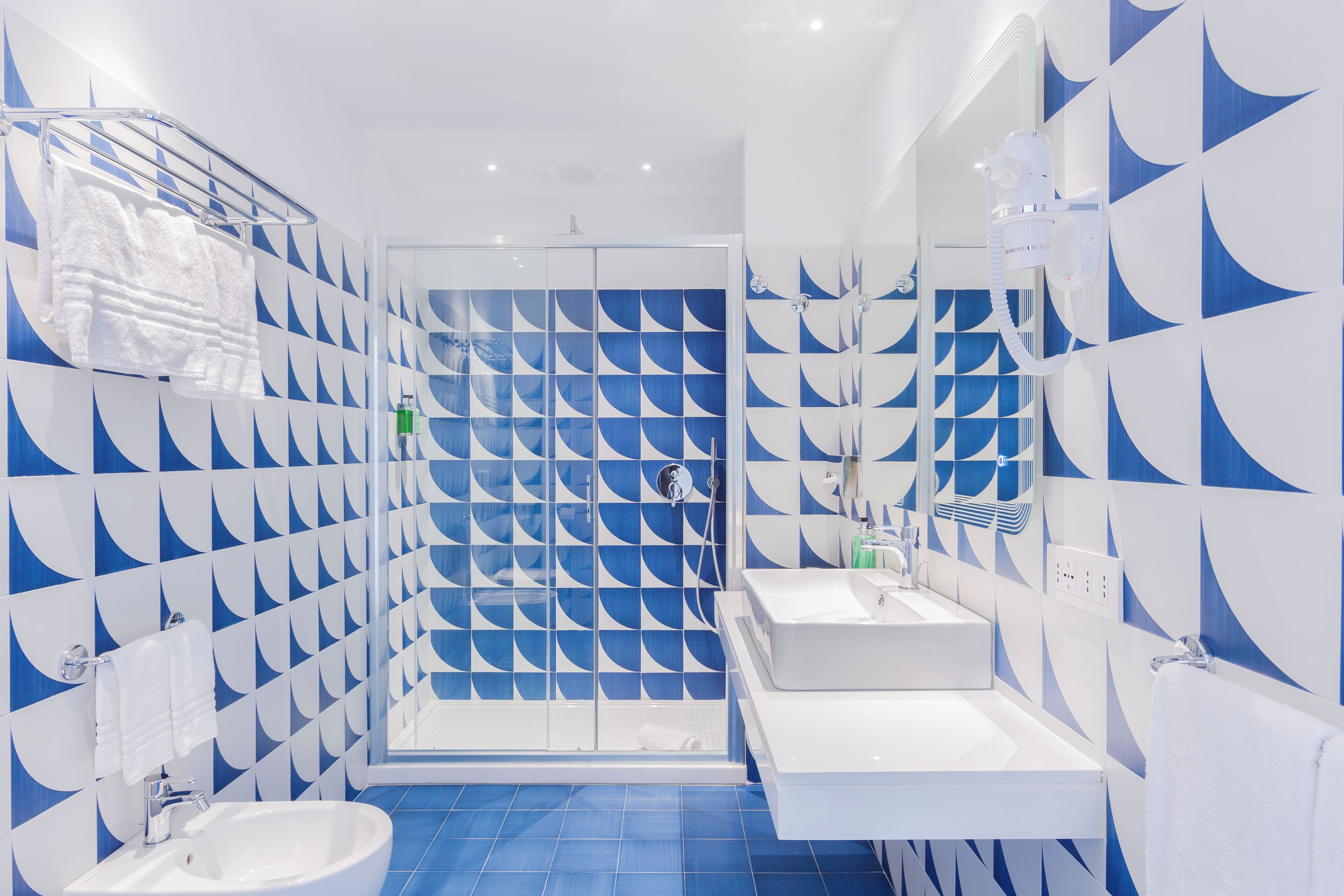 Een moderne badkamer met een geometrisch tegelpatroon, een glazen douchecabine en een witte wastafel.