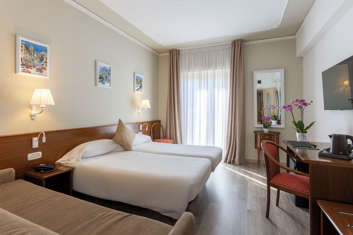 A hotel room with two beds, a desk with a chair, a TV, and artwork on the walls.