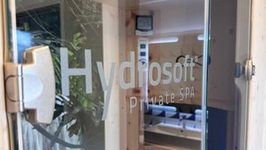 Une salle de spa privée dotée d’une porte en verre, d’un plafond orné de luminaires circulaires et d’un élément décoratif aquatique visible à l’extérieur.