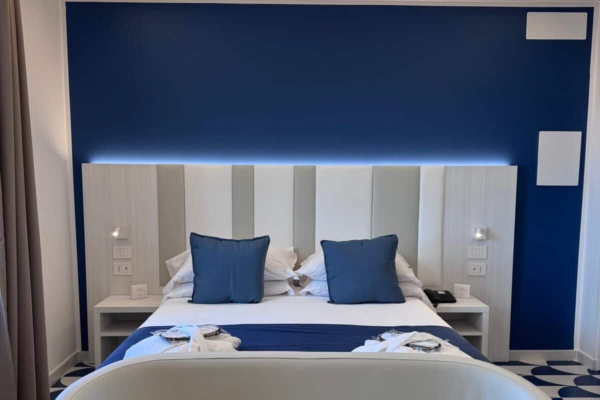 A hotel room with a bed, bedside tables, a chair, and a blue accent wall.