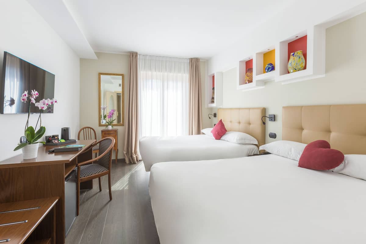 A hotel room with two beds, a desk, a chair, a TV, and a mirror.