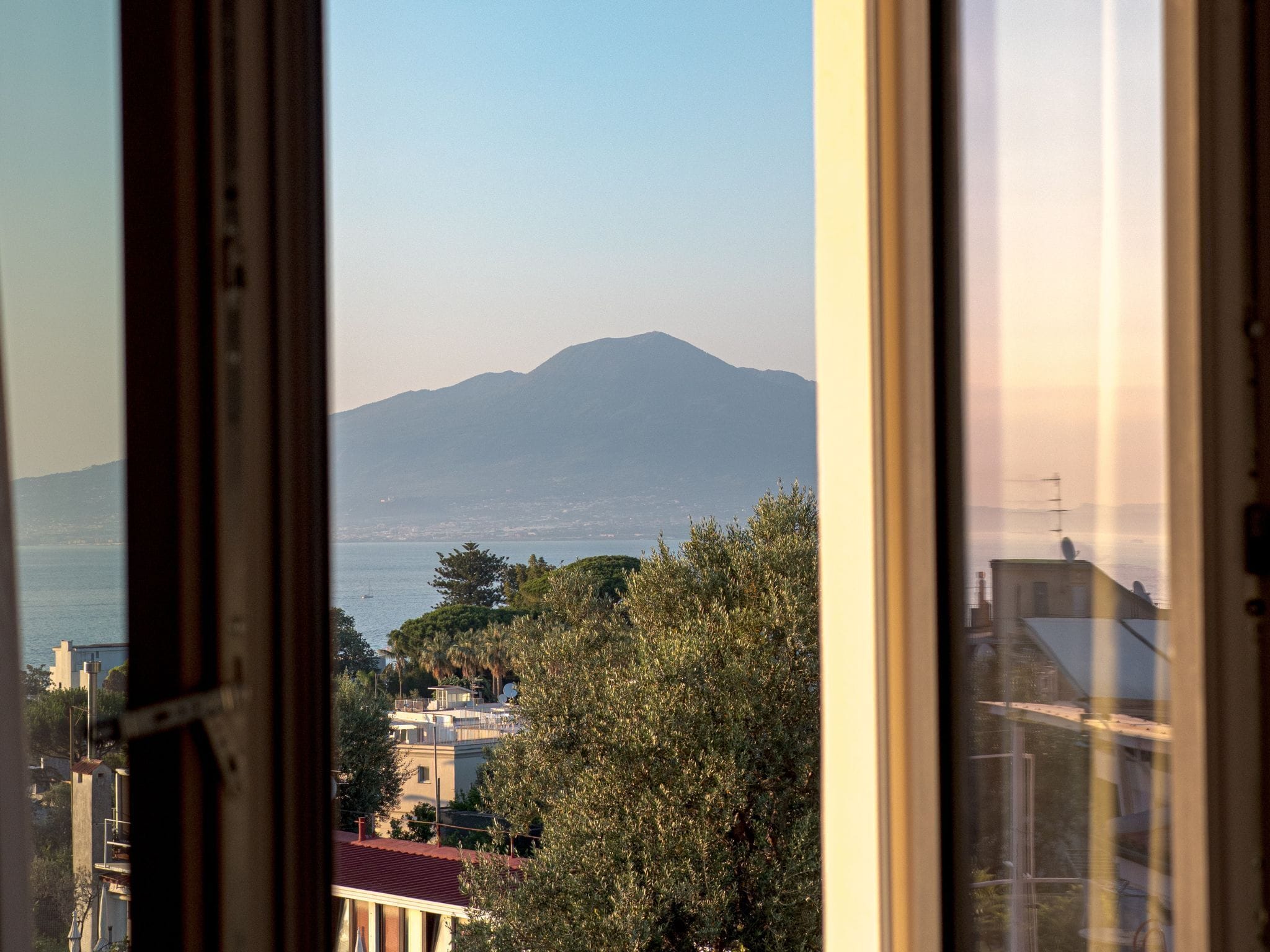 Une vue à travers une fenêtre, avec une montagne au loin, une étendue d’eau et des bâtiments.