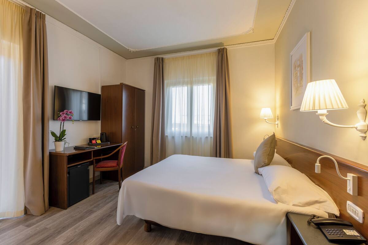 A hotel room with a bed, desk, chair, TV, and a lamp.