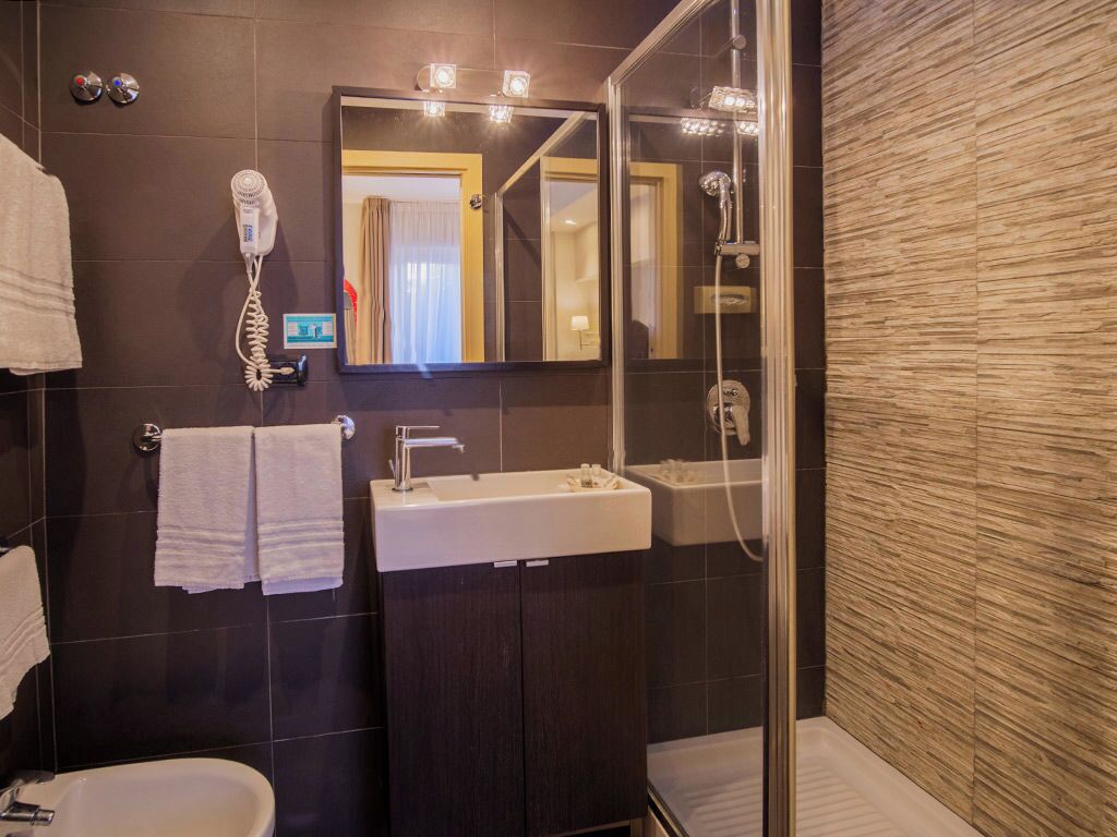 Une salle de bain moderne avec un mur recouvert de carreaux foncés, un grand miroir, un lavabo, une douche et un sèche-cheveux.