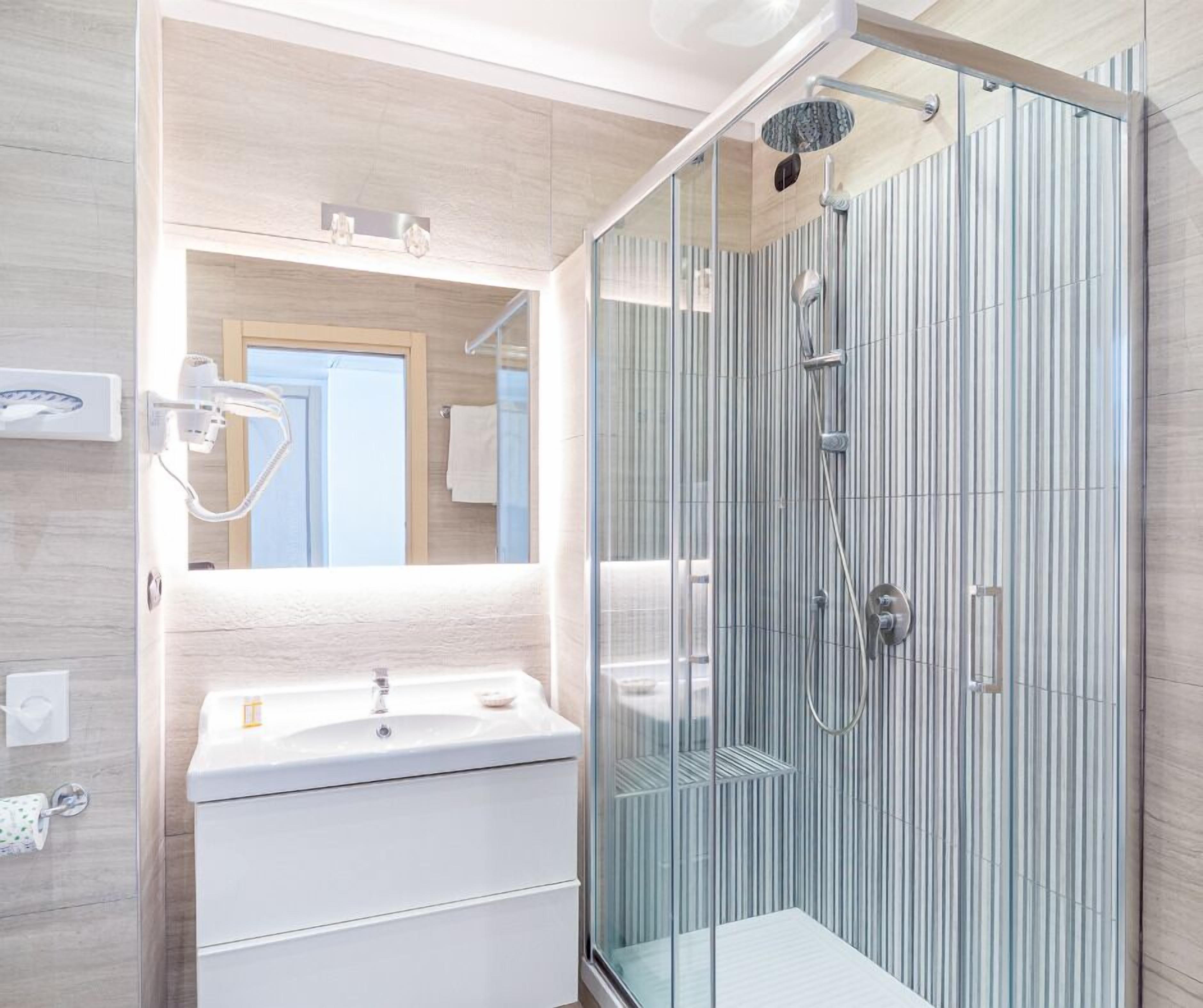 Un baño moderno con ducha de vidrio, un espejo grande y un tocador blanco.