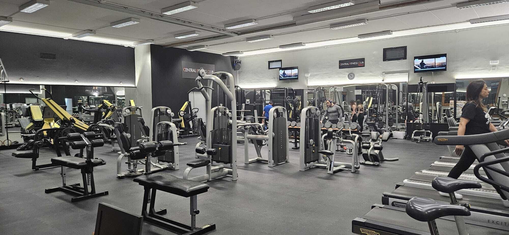 Ein Fitnessstudio mit verschiedenen Trainingsgeräten, Spiegeln und einem Fernseher an der Wand.