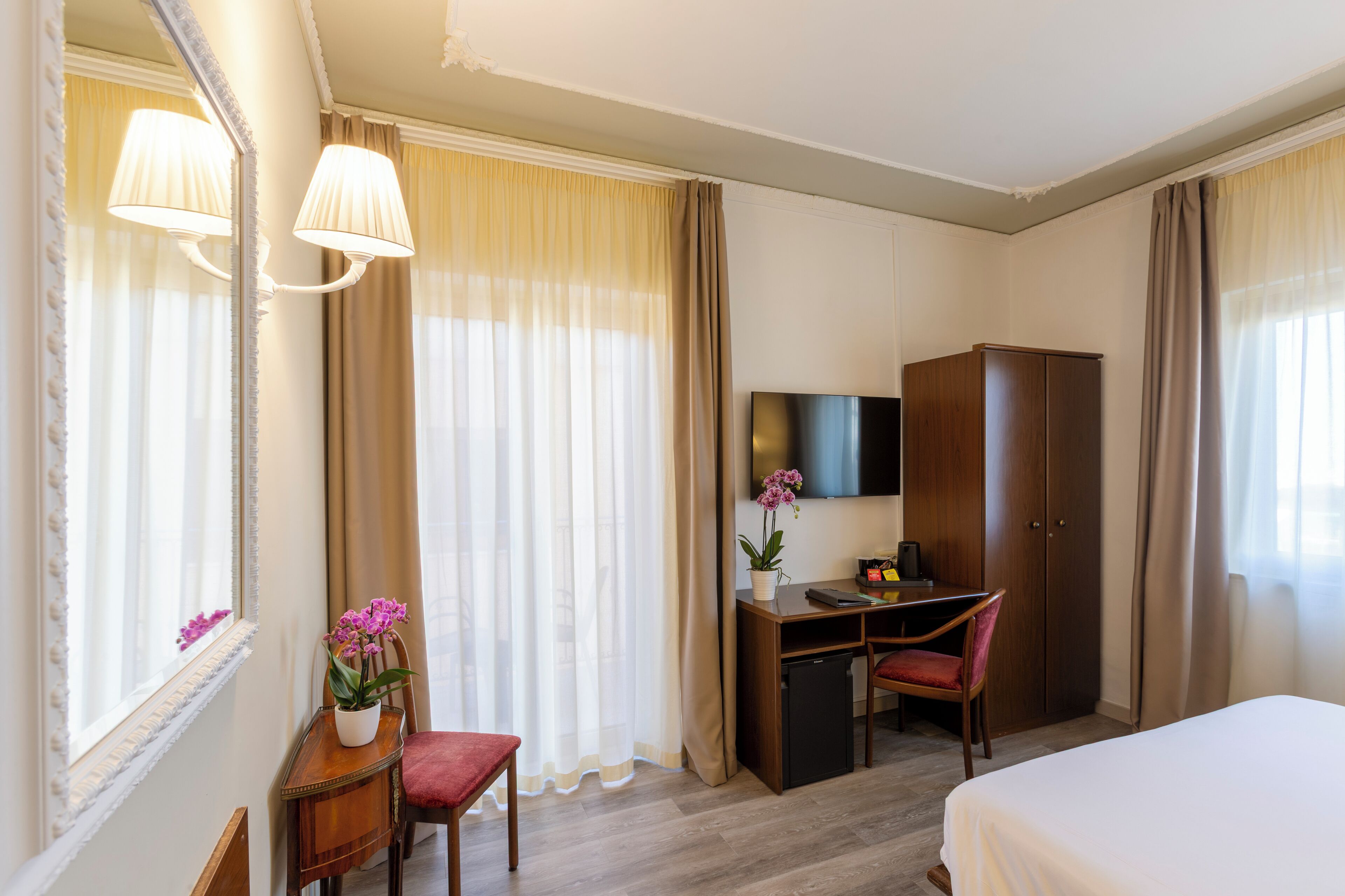 Een hotelkamer met een bed, een bureau met stoel, een televisie, een kledingkast en een raam met gordijnen.