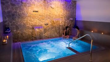 A spa area with a stone wall, a hot tub, and a person sitting by the tub.