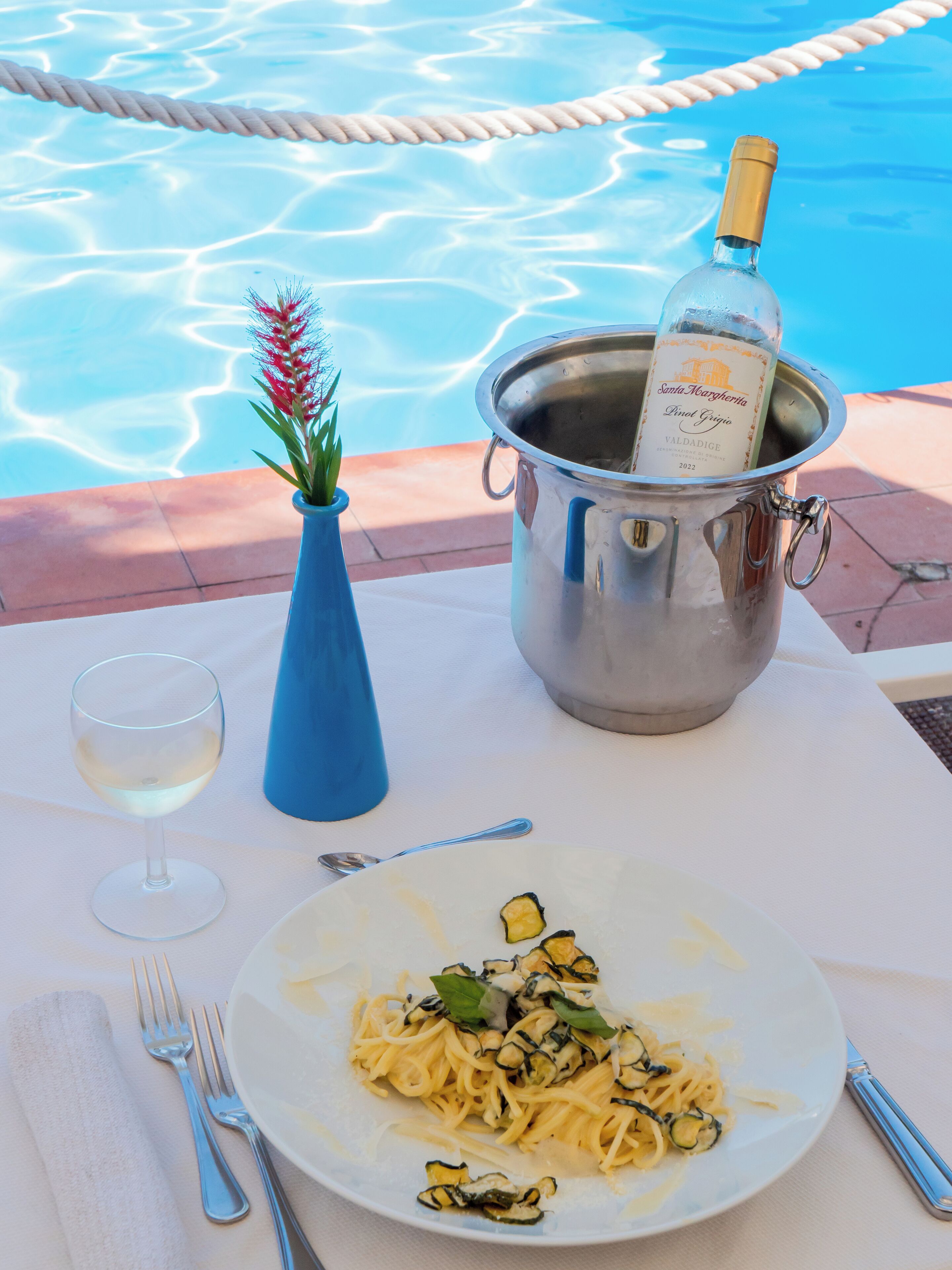 A dining table with a plate of pasta, a wine glass, and a bottle of wine in a metal bucket.