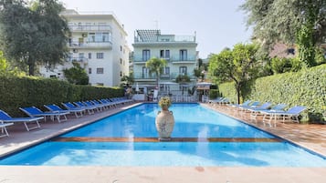 A swimming pool with lounge chairs and a large vase in the center.
