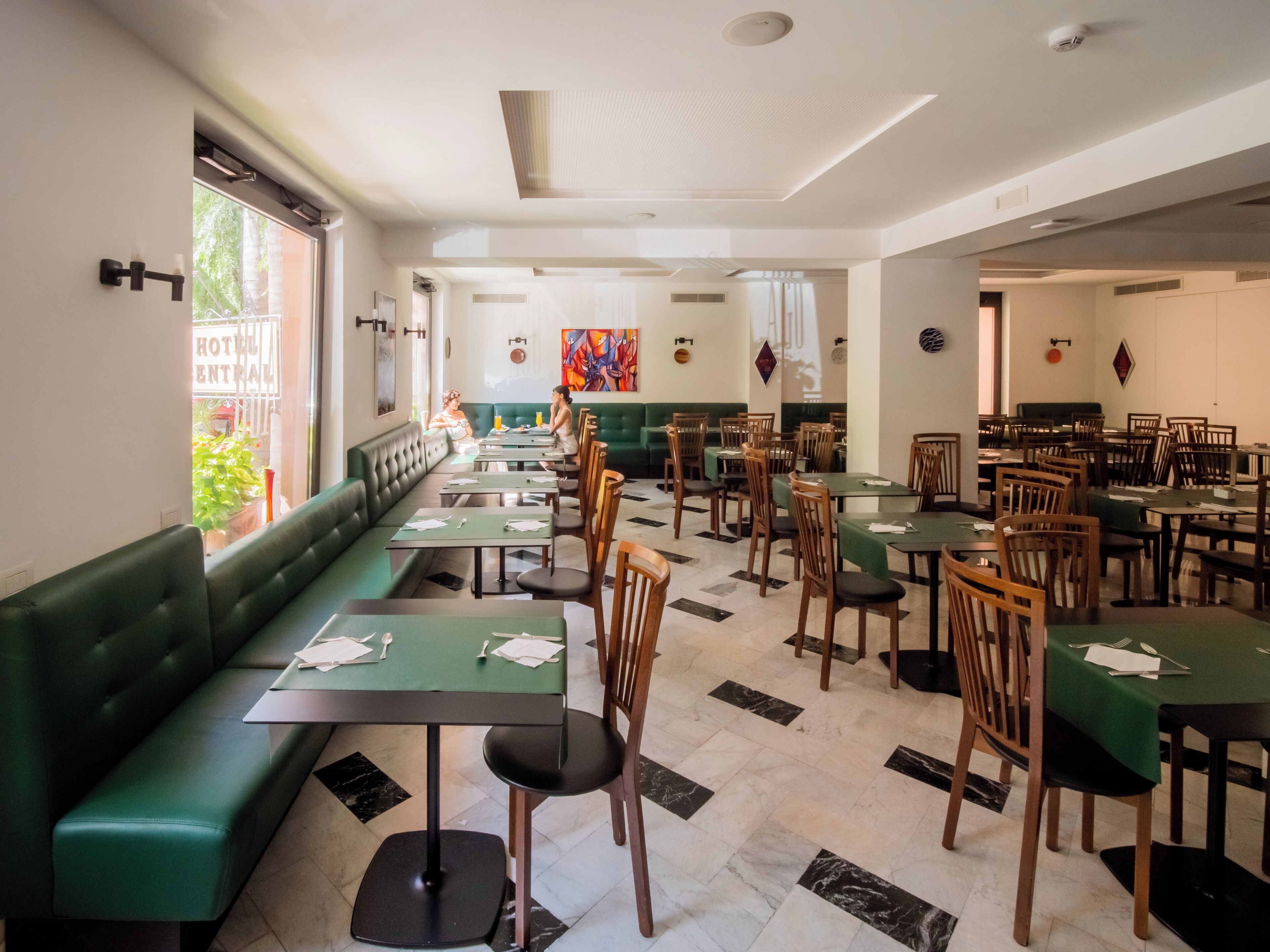Un restaurant spacieux avec des banquettes vertes et des tables en bois, un sol carrelé et une vue sur l’extérieur.