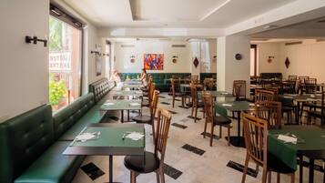 Un restaurant spacieux avec des banquettes vertes et des tables en bois, un sol carrelé et une vue sur l’extérieur.