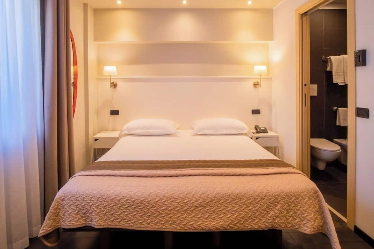 A hotel room with a large bed, bedside lamps, a telephone, and a view of the bathroom.