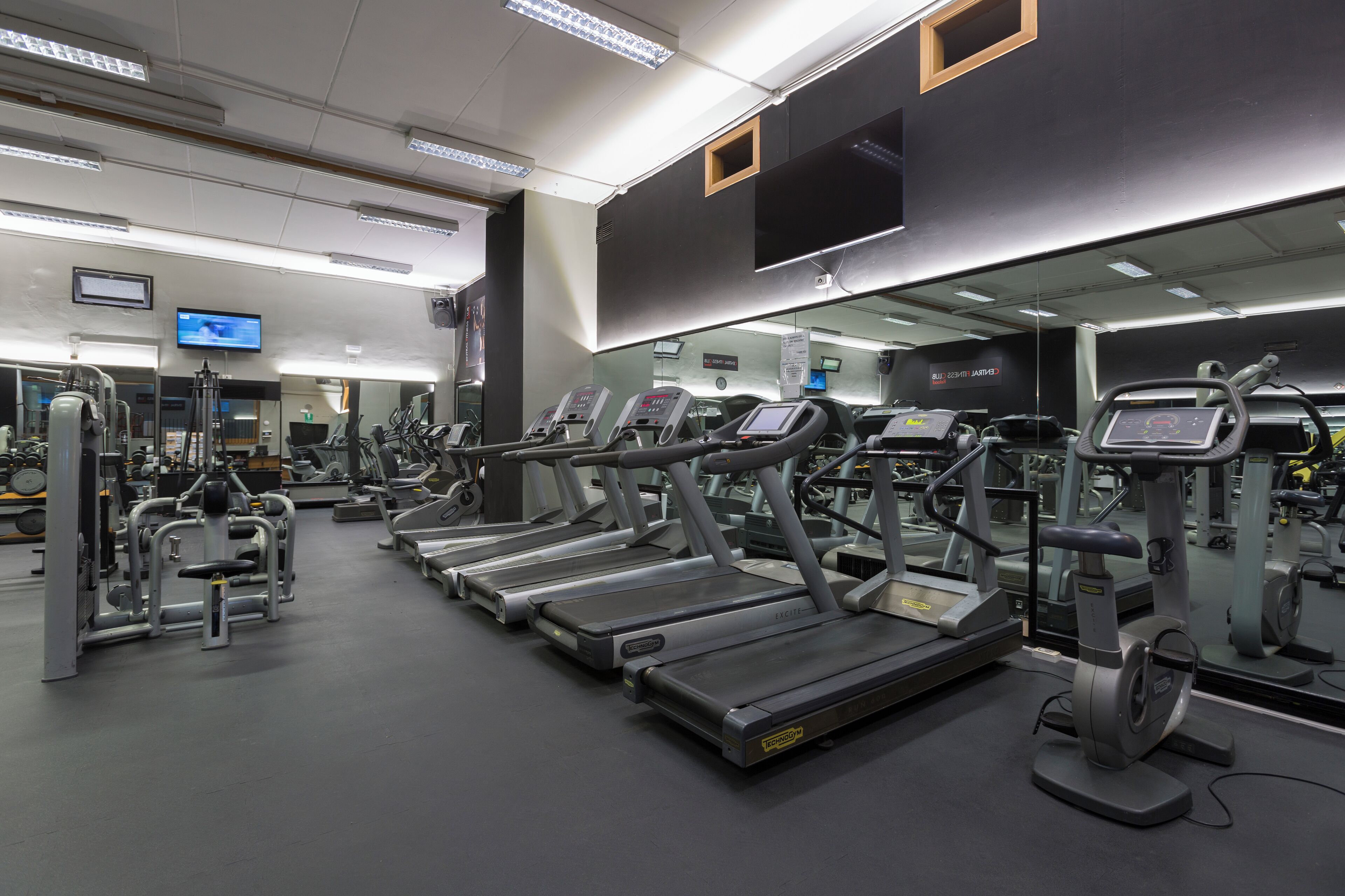 Un gimnasio con cintas de correr, máquinas de pesas y un espejo grande.