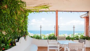Une terrasse avec un banc blanc aux lignes courbes, une table et des chaises, offrant une vue sur la côte.
