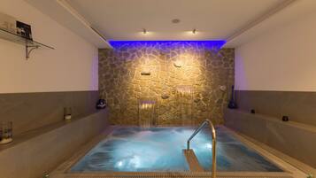 Zona de spa con pared de piedra, jacuzzi y estante de vidrio con objetos.