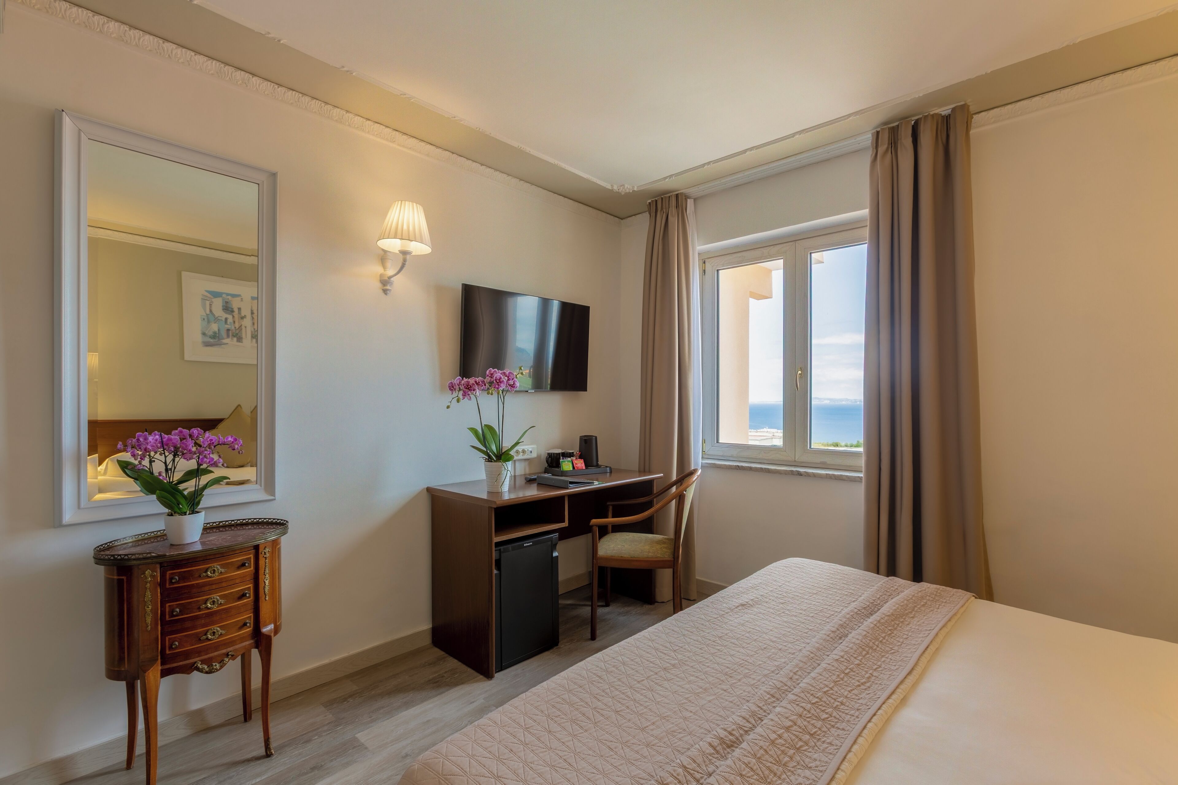 A hotel room with a bed, desk, chair, TV, and a window with curtains.