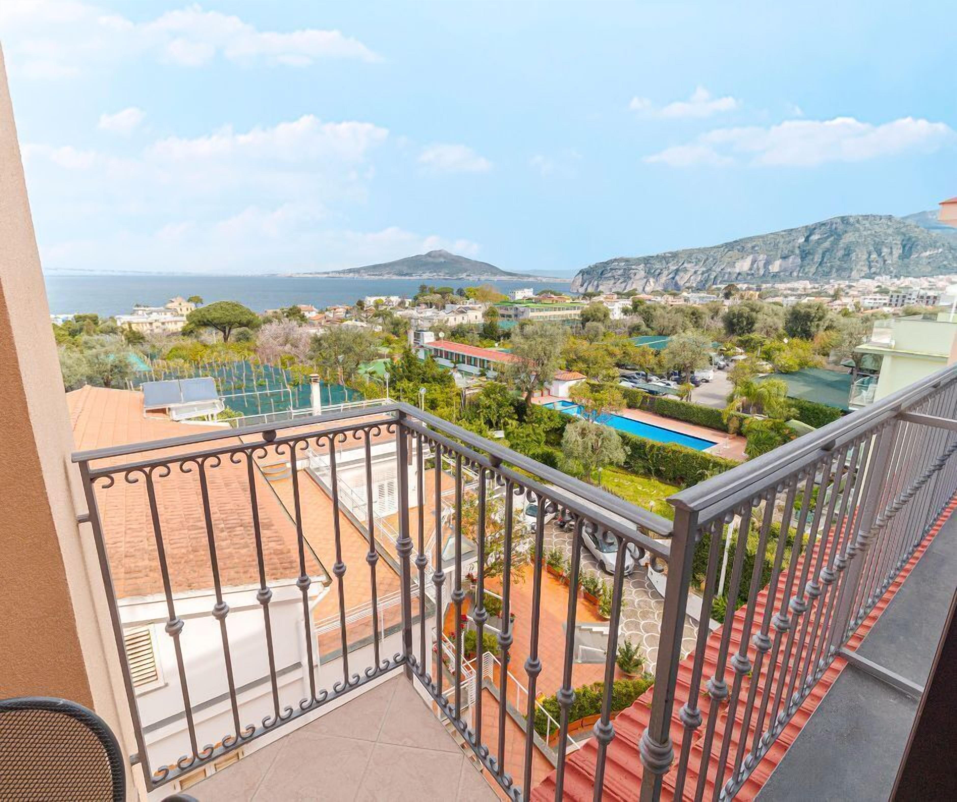 A balcony with a view of a swimming pool, greenery, and distant mountains.