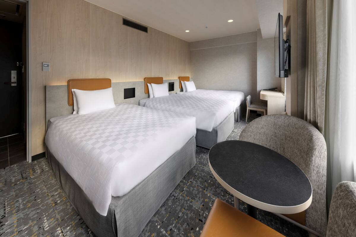 A hotel room with two beds, a desk, a chair, and a TV.