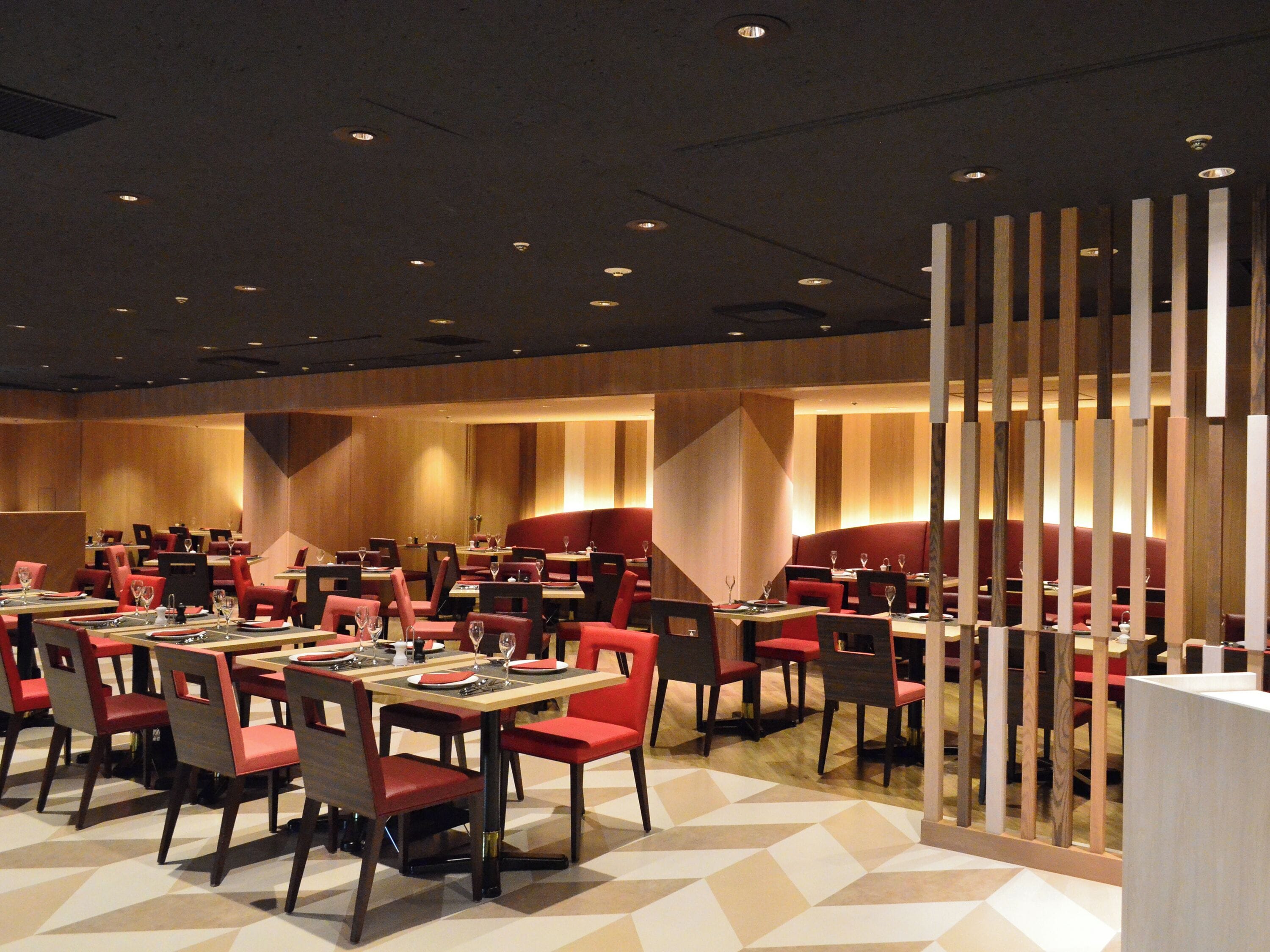 A modern restaurant with multiple tables and booths, featuring geometric patterned flooring and warm lighting.