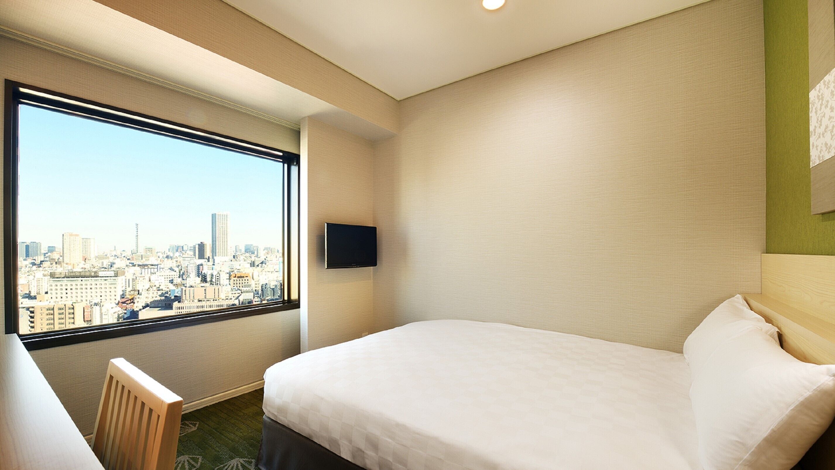 A hotel room with a bed, a desk, a chair, a TV, and a city view.
