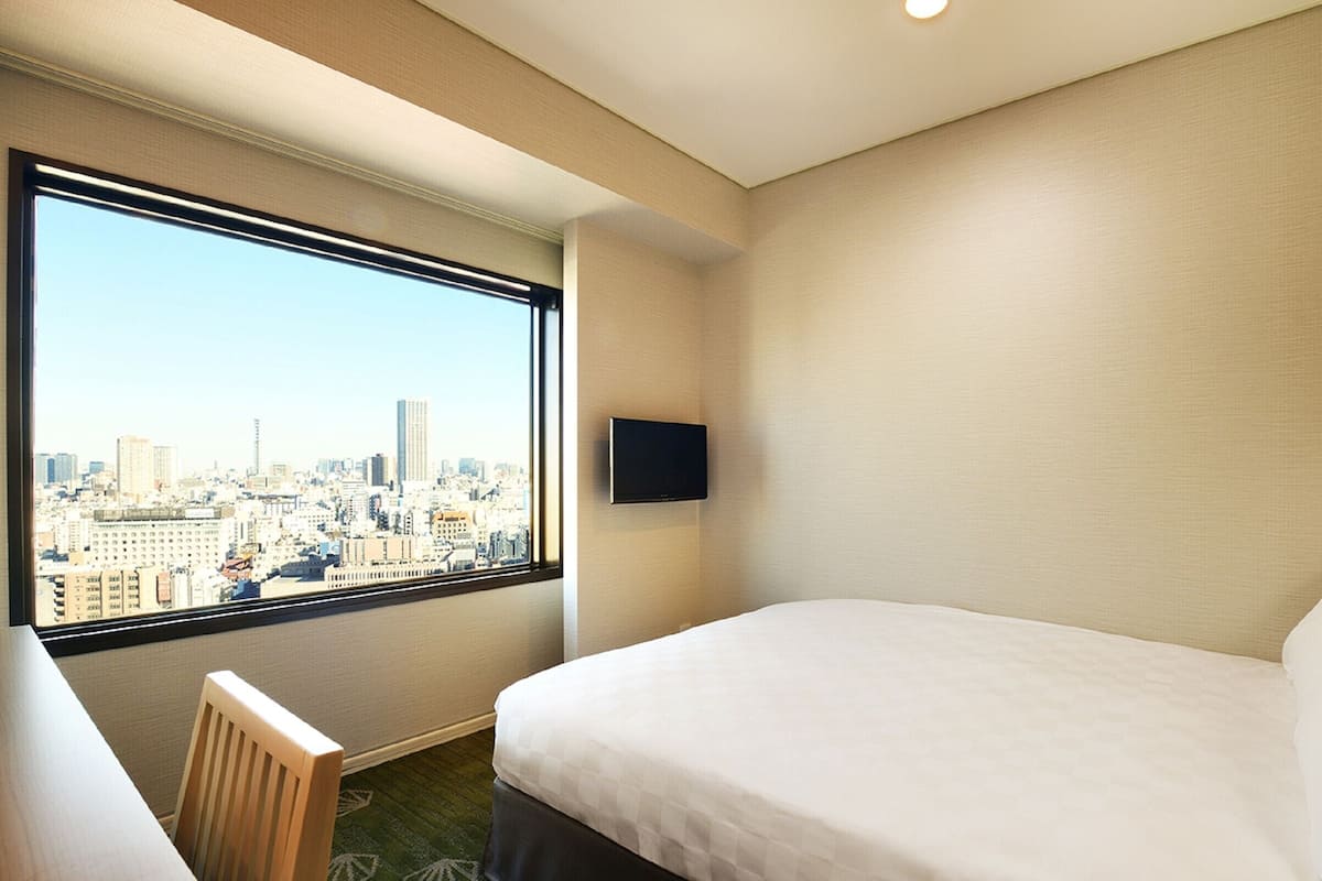 A hotel room with a bed, a desk, a chair, a TV, and a city view.