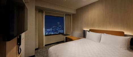 Une chambre d’hôtel avec un grand lit, une télévision, un bureau et une fenêtre donnant sur la ville.