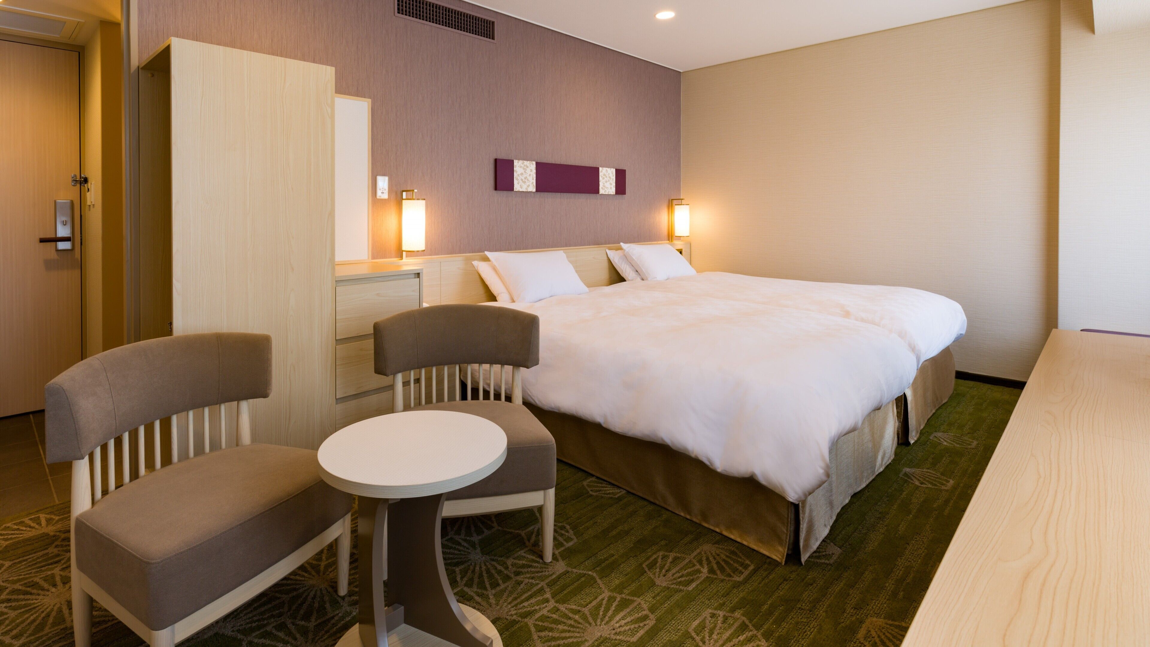 A hotel room with a bed, two chairs, a small table, a dresser, and a mirror.