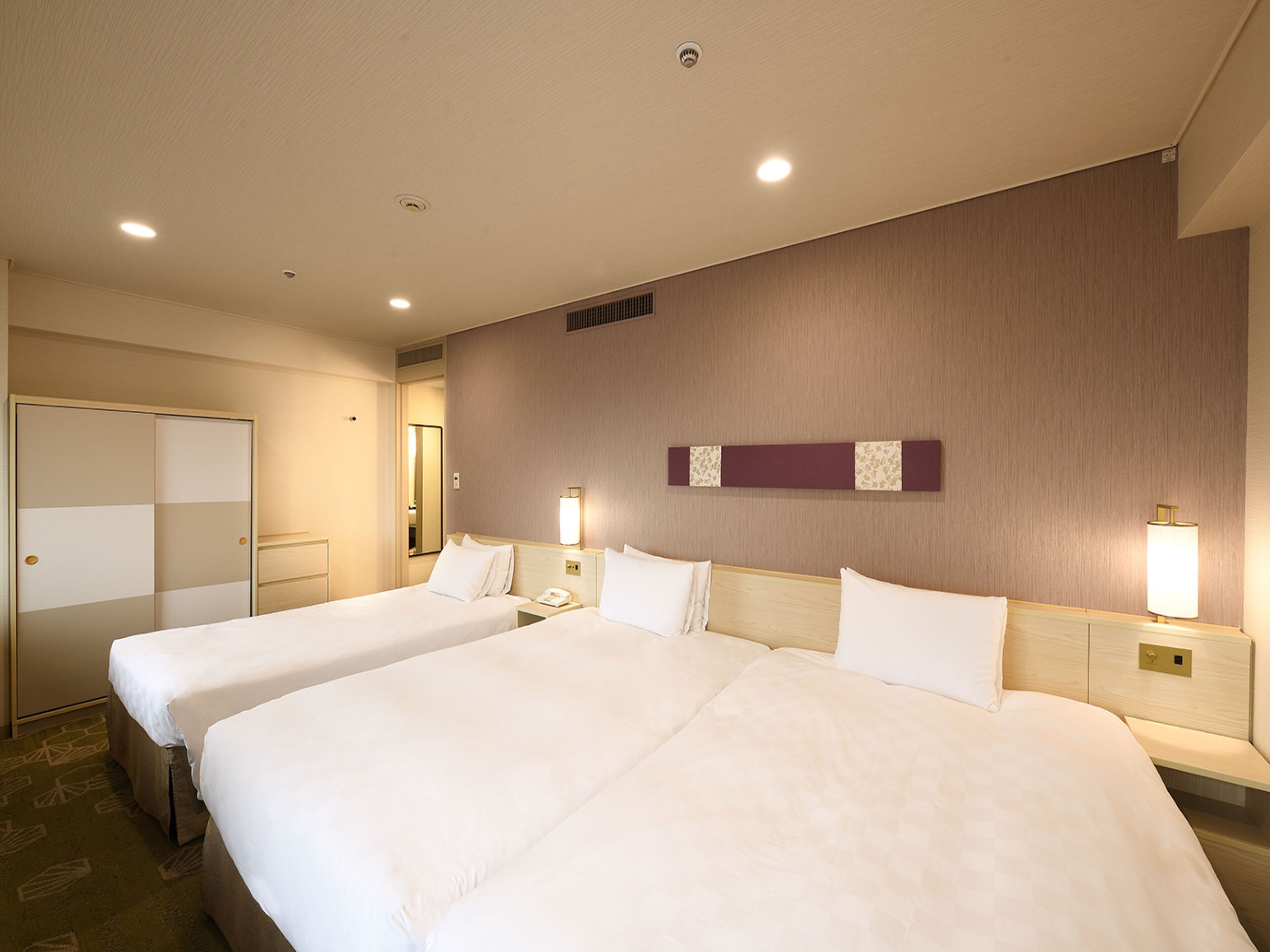 A hotel room with two beds, a wardrobe, a mirror, and a wall-mounted light fixture.