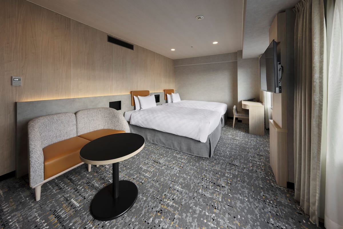 A modern hotel room with a large bed, a sofa, a small table, and a TV.