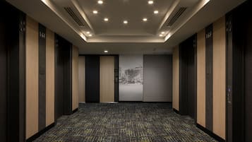 A modern elevator lobby with a patterned carpet, recessed lighting, and a large wall-mounted advertisement.