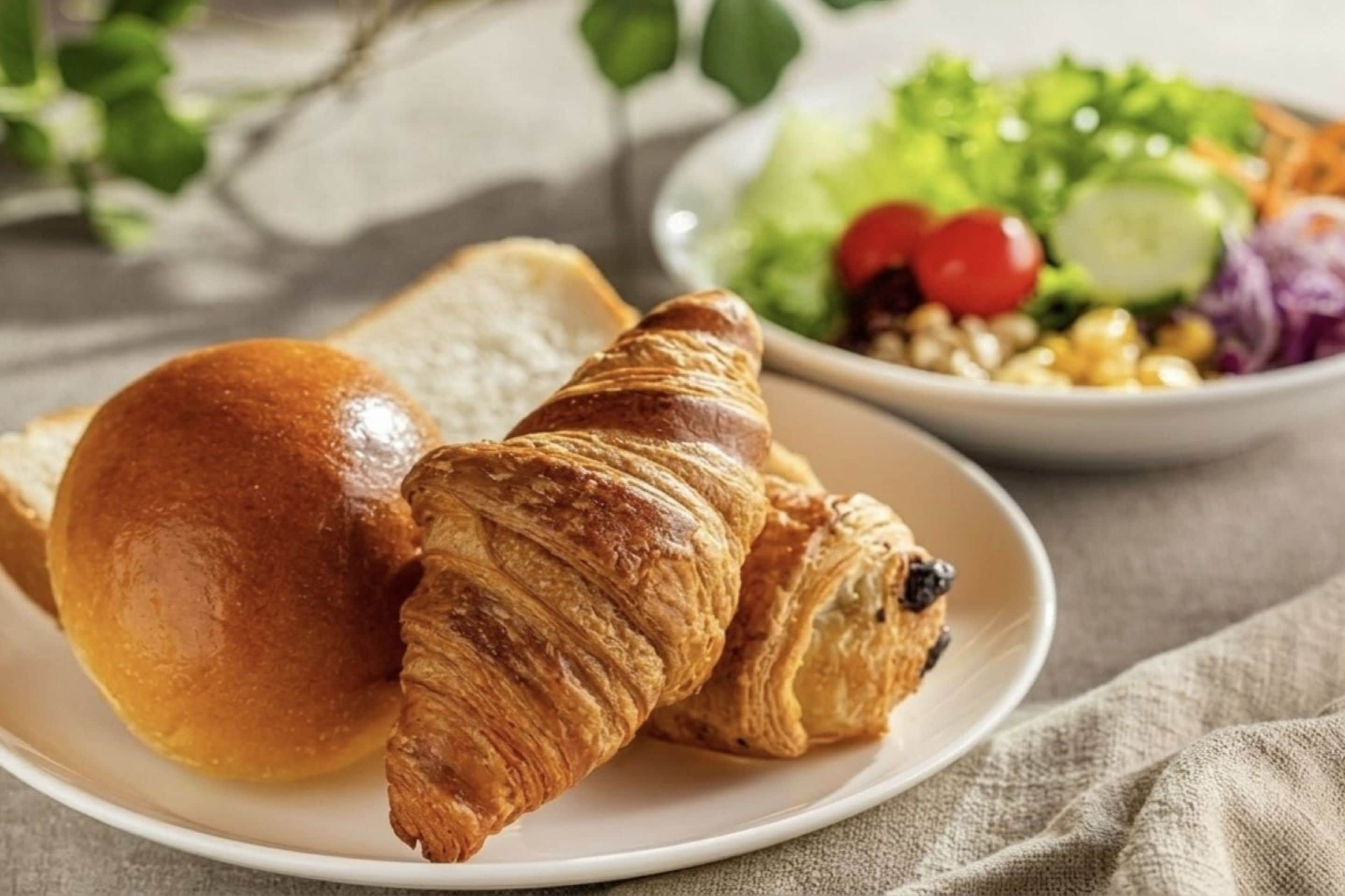 Une assiette avec un croissant et un pain, et un saladier de salade composée avec des légumes.