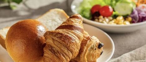 Een bord met een croissant en een broodje, en een saladekom met groenten.